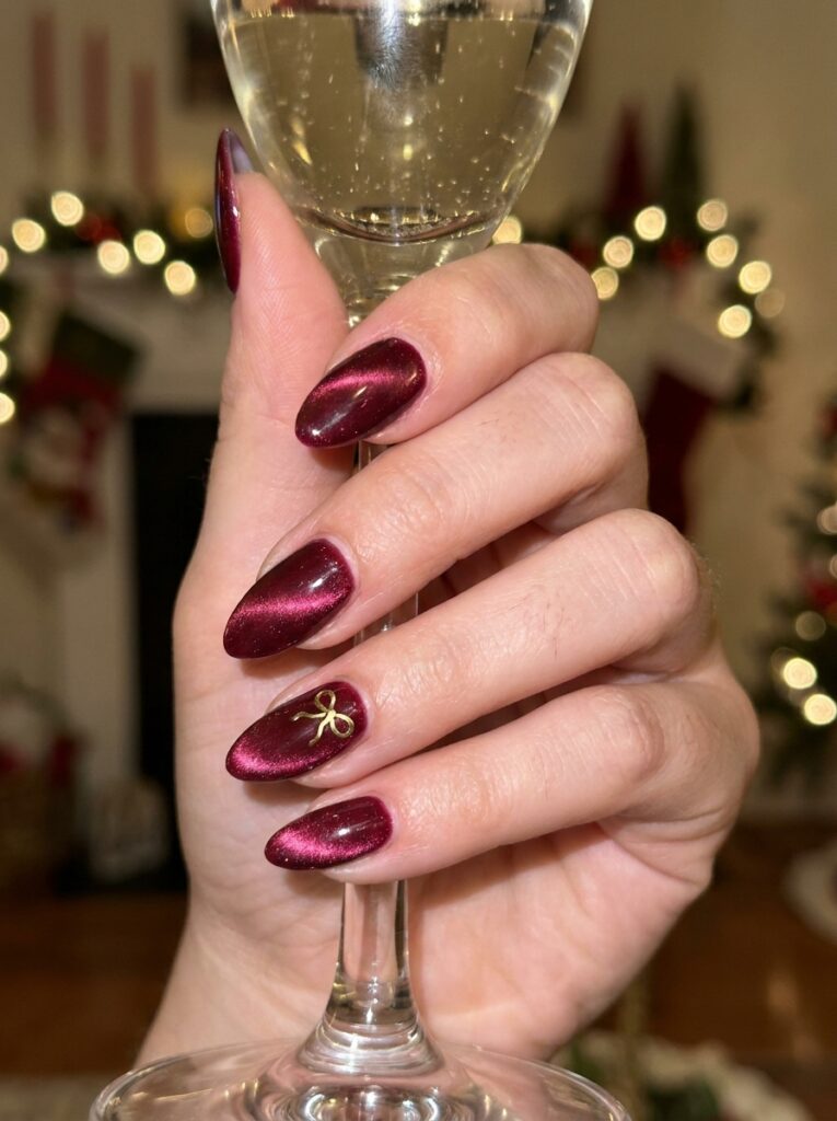cranberry velvet cat eye christmas nails with a gold bow